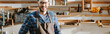 © LIGHTFIELD STUDIOS - panoramic shot of cheerful carpenter in apron looking at camera in workshop