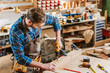 © LIGHTFIELD STUDIOS - woodworker in goggles and apron holding hammer drill near wooden planks