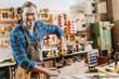 © LIGHTFIELD STUDIOS - happy woodworker in goggles and apron holding hammer drill near wooden planks