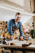 © LIGHTFIELD STUDIOS - selective focus of cheerful woodworker holding pencil near planks