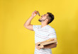 Handsome man eating tasty pizza on yellow background
