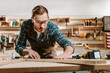 © LIGHTFIELD STUDIOS - selective focus of handsome carpenter in goggles touching wooden plank