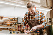 © LIGHTFIELD STUDIOS - bearded carpenter holding chisel while carving wood in workshop