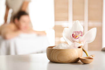 Bowl with sea salt and orchid flower on white table in spa salon. Space for text