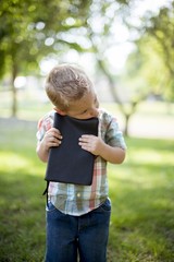 Wall Mural - Vertical shot of a child holding the bible against his chest with a blurred natural background