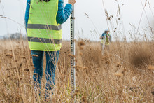 Cropped View Of Surveyors With Survey Ruler And Digital Level In Field