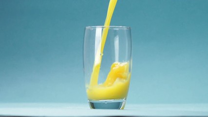 Wall Mural - orange juice is poured into a glass on blue background