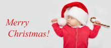 Christmas Card Or Banner With A Newborn Sleeping Baby In A Santa Claus Hat, Red-and-white Clothes And A Candy Сane In A Small Hand. The Inscription "Merry Christmas!"