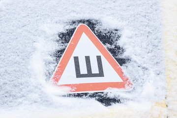 Car sticker studded tires on the snow-covered rear glass of the car in the winter. Russian warning sign