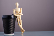 Wooden Man Figure With Cardboard Cup Of Coffee On Gray Background