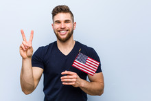 Young Caucasian Man Holding A United States Flag Showing Number Two With Fingers.
