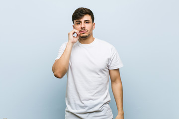 Wall Mural - Young caucasian man wearing a white tshirt with fingers on lips keeping a secret.