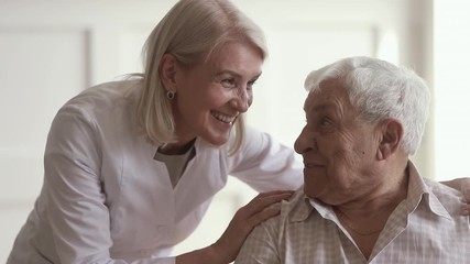 Wall Mural - Smiling mature kind woman nurse talking to disabled elder man