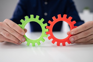 Businessperson Joining Gears On Desk