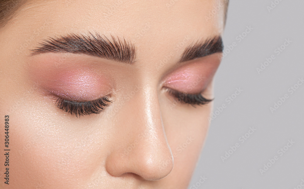 Beautiful young woman with long eyelashes, beautiful fresh nude make-up, thick eyebrows and with clean skin in a beauty salon. Eyelash extensions. Eyebrows close up. Make-up concept. - obrazy, fototapety, plakaty 