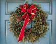 Christmas wreath with large red bow trimmed in gold hanging on old wooden blue door