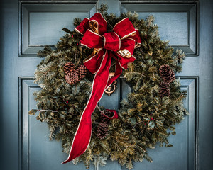 Christmas wreath with large red bow trimmed in gold hanging on old wooden blue door