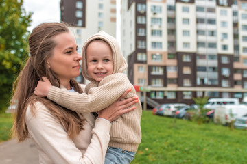 Young happy family, woman mom and little son boy. Hug in autumn on street, smiling for a walk and rejoice. Casual warm clothes with a hood jumper. Free space for copy text.