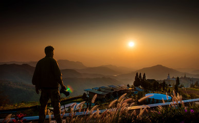 Wall Mural - silhouette a man with a camera looking at the sunrise in the morning on the hill