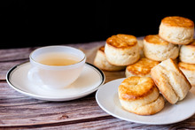 White Cup Of Hot Tea And Fresh Homemade Delicious Butter Scones On Wooden Table With Black Background. Traditional British Scones Perfect Combination For Tea Time.