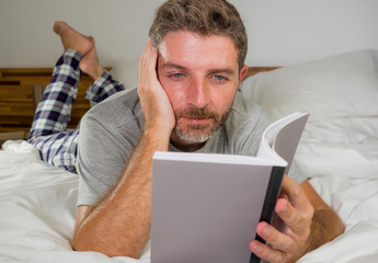 Wall Mural - lifestyle portrait of young attractive and relaxed man at home lying comfortable on bed wearing  pajamas reading a book enjoying an interesting novel chilled and cozy