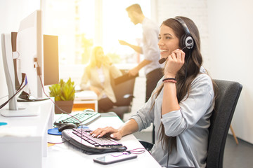 Smiling businesswoman or helpline operator with headset using computer at office