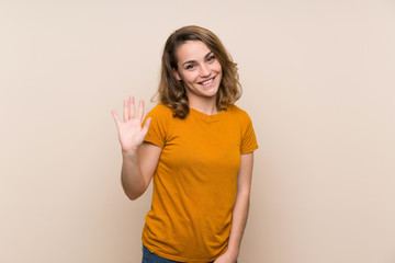 Wall Mural - Young blonde girl over isolated background saluting with hand with happy expression