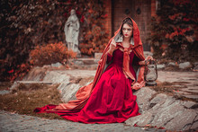 Beautiful Girl In A Burgundy Coat And Red Dress Sitting On The Background Of The Castle In The Park, October