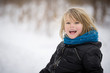 © goodmoments - Portrait of an adorable little kid boy with long blond hair in a park. A child in a black jacket with a blue scarf having fun on a winter snowy day.