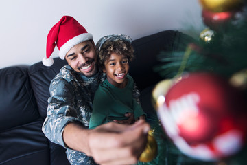 Soldier decorating Christmas tree with his daughter. An off duty military man spending Christmas holiday with his family at home.