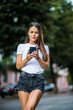 Young Woman walking and using a smart phone in the street in a sunny summer day