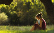 © fantom_rd - sunny portrait of a beautiful girl sitting on green glade under tree branches with book, woman reading novel on nature, concept hobby and lifestyle