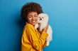 © wayhome.studio  - Studio shot of glad female model holds fluffy pet closely to face after grooming, smiles with happiness, cares about pedigree animal, being on friendly terms with dog, poses against blue background.