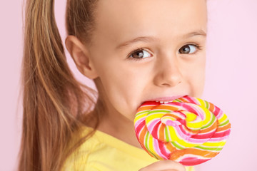 cute little girl with sweet lollipop on color background