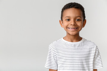 Little African-American boy with hearing aid on light background