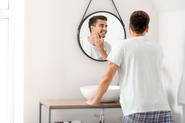 Handsome young man looking in mirror after shaving at home