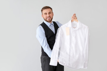 Poster - Male worker of modern dry-cleaner's with clothes on light background