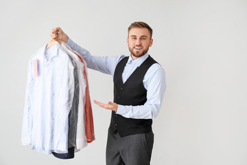 Poster - Male worker of modern dry-cleaner's with clothes on light background