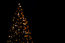 Lights Of Christmas Tree Blurred Bokeh On Dark Background With Copy Space.