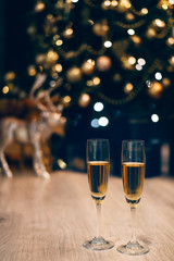 Two glasses of champagne standing on the blurred decorated christmas tree background.