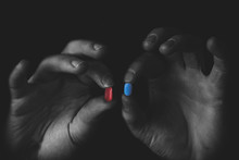 Man Holding Red And Blue Pills In Hand Isolated On Black Background.  Medicine Concept And Pills, Copy Space