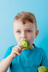 Wall Mural - Little kid holding broccoli in his hands on blue background. Vegan and healthy concept