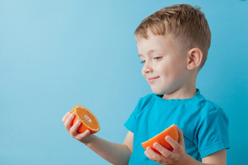 Wall Mural - Little Boy Holding an Orange in his hands on blue background, diet and exercise for good health concept