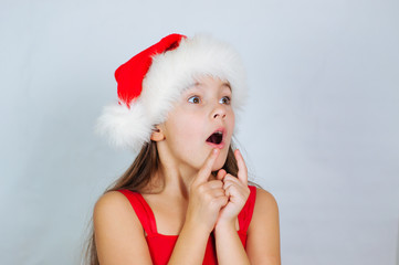 Wall Mural - little cute girl is standing in a Christmas hat and surprised at the holiday