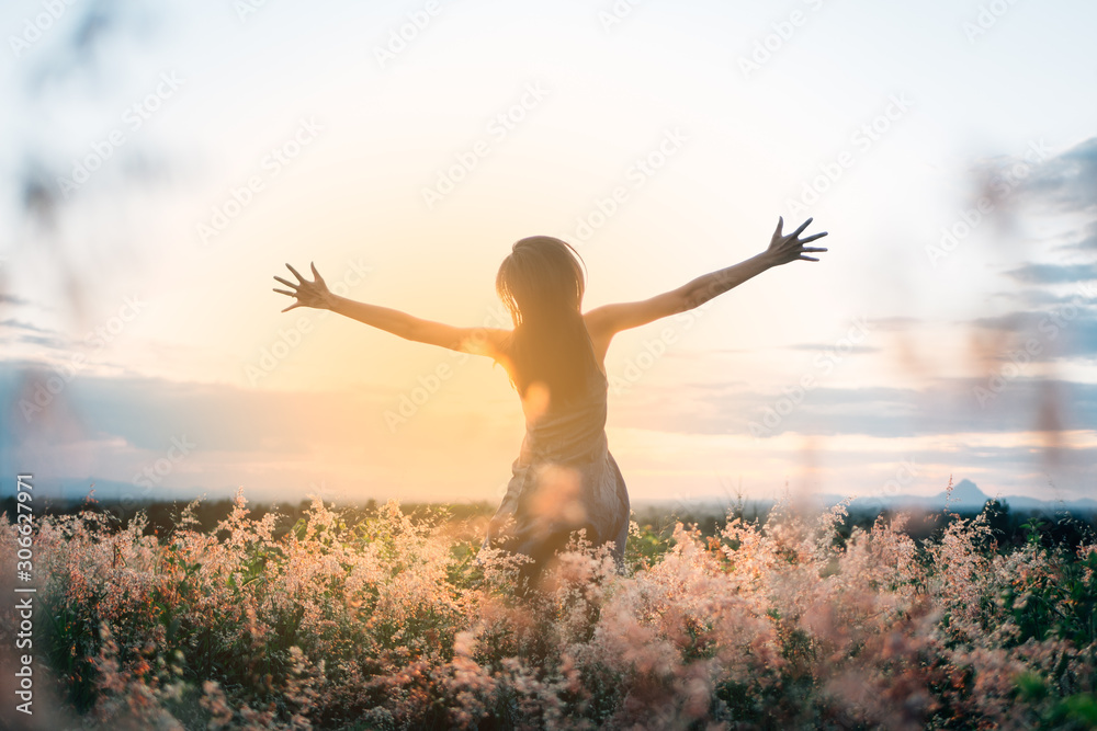 Trendy girl in stylish summer dress feeling free in the field with flowers in sunshine.