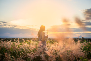 Trendy girl in stylish summer dress feeling free in the field with flowers in sunshine.