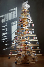 Eco-friendly Creative Christmas Tree Made Of Boards. Alternative Christmas Tree Decorated With Toys For The New Year . In A Dark Room, In The Light From The Window .