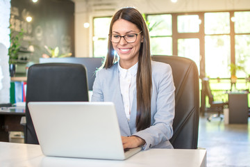 Young businesswoman in formal wear working on laptop in bright office.