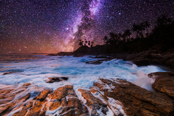 Tropical beach with palm trees under starry sky with Milky Way.