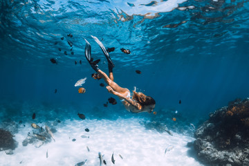 freediver girl with fins glides over sandy bottom with fishes in blue ocean